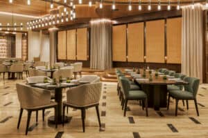 Un restaurante moderno y elegante con un interior sofisticado, sillones acolchados, mesas elegantemente decoradas, detalles en madera e iluminación tenue, ideal para conferencias o reuniones. El ambiente es cálido y acogedor, reflejando el estilo de los mejores hoteles y resorts de México.