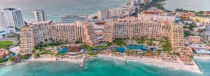 Vista aérea de un gran complejo turístico frente al mar en México, con varias piscinas, palmeras, tumbonas y acceso directo al océano, perfecto para reuniones o eventos de conferencias, ubicado a lo largo de una concurrida costa con hoteles de gran altura al fondo.