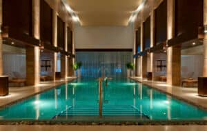 Lujosa piscina cubierta de agua turquesa, rodeada de elegantes columnas, iluminación cálida y tumbonas: perfecta para relajarse después de eventos y conferencias en hoteles y resorts de lujo en México.
