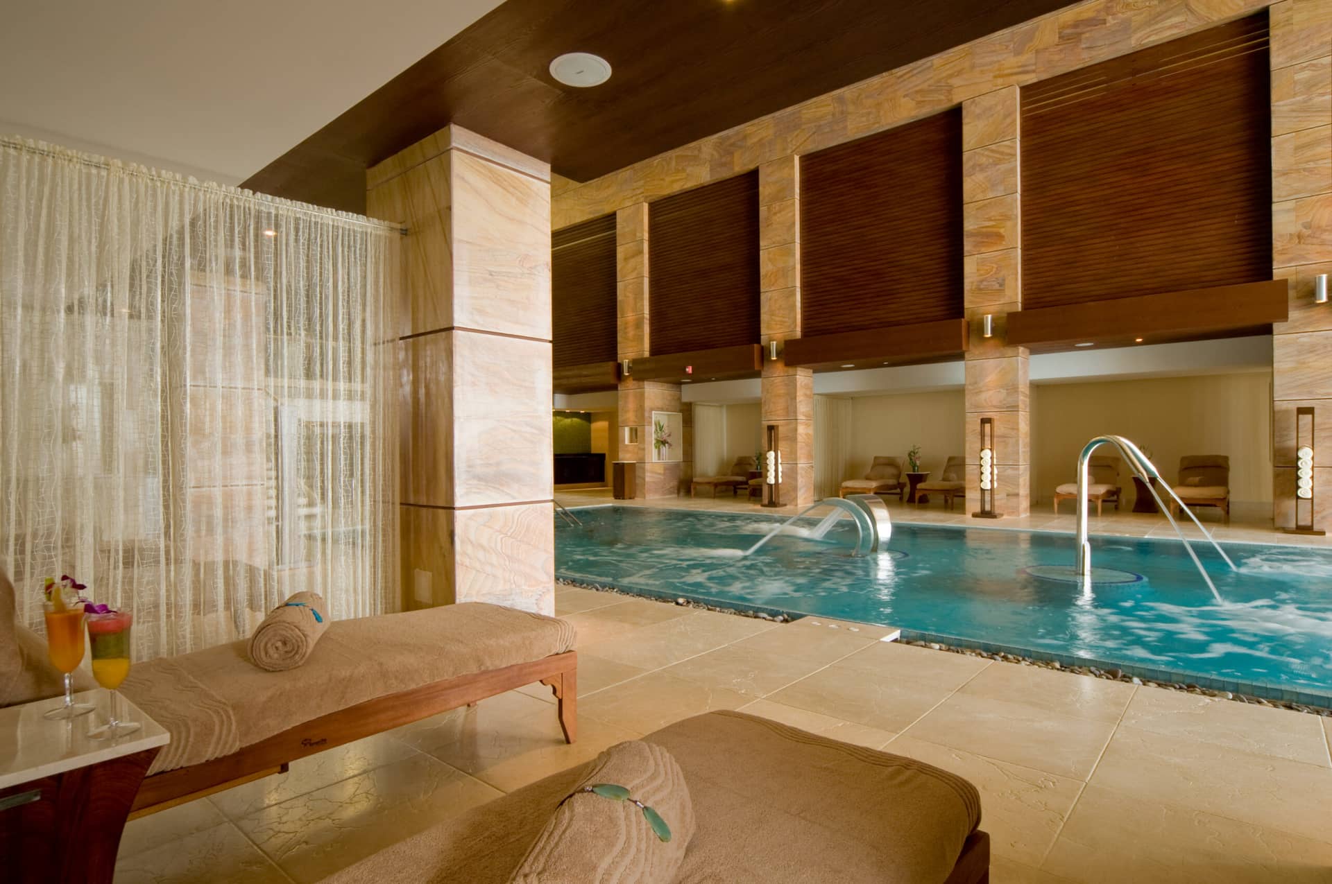 A luxurious indoor spa at one of Mexico’s finest resorts, featuring a turquoise pool, lounge chairs with rolled towels, drinks on side tables, and soft lighting—perfect for relaxation after conference events or meetings.