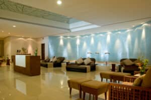 Un moderno salón de spa con cómodos asientos, una recepción de madera y una pared decorativa azul texturizada con pequeñas fuentes de agua: ideal para huéspedes de resorts en México o eventos de conferencias. La iluminación tenue y las flores frescas crean un ambiente relajante.