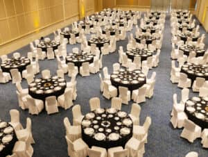 Un gran salón de banquetes en un complejo turístico de México, dispuesto con mesas redondas cubiertas con manteles negros, cada una rodeada de fundas blancas para sillas y con platos y vasos, listo para eventos formales, reuniones o conferencias.