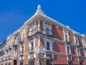 Edificio histórico ornamentado con paredes de ladrillo rojo con motivos decorativos y molduras blancas, que cuenta con balcones y elaborados detalles arquitectónicos, perfecto para eventos o reuniones en los mejores hoteles de México, con un cielo azul despejado de fondo.
