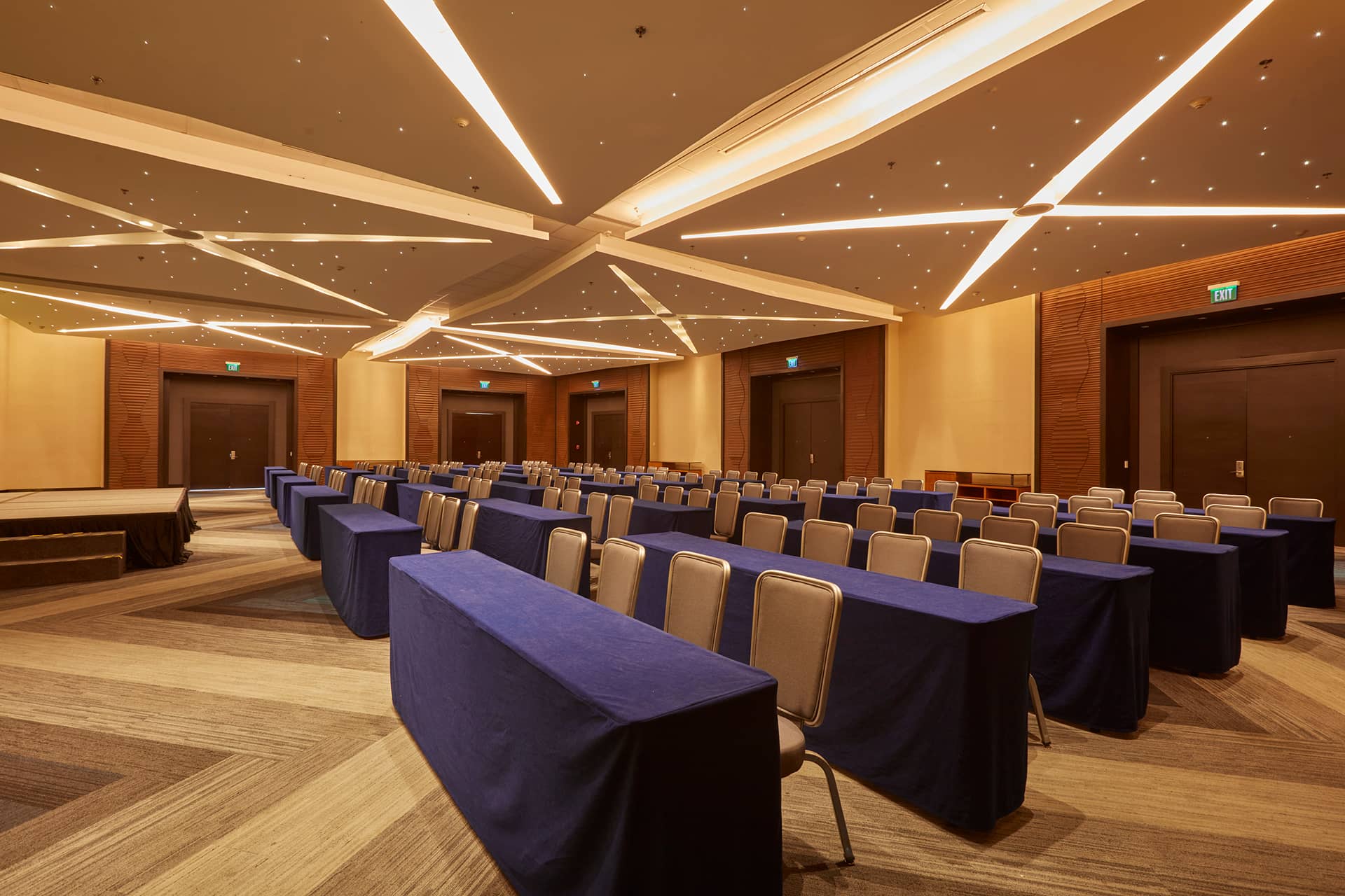 Rows of tables with blue tablecloths and beige chairs are set up in a spacious, modern conference room at one of Mexico’s premier resorts—perfect for meetings or conference events, with stylish ceiling lights and wooden accents.
