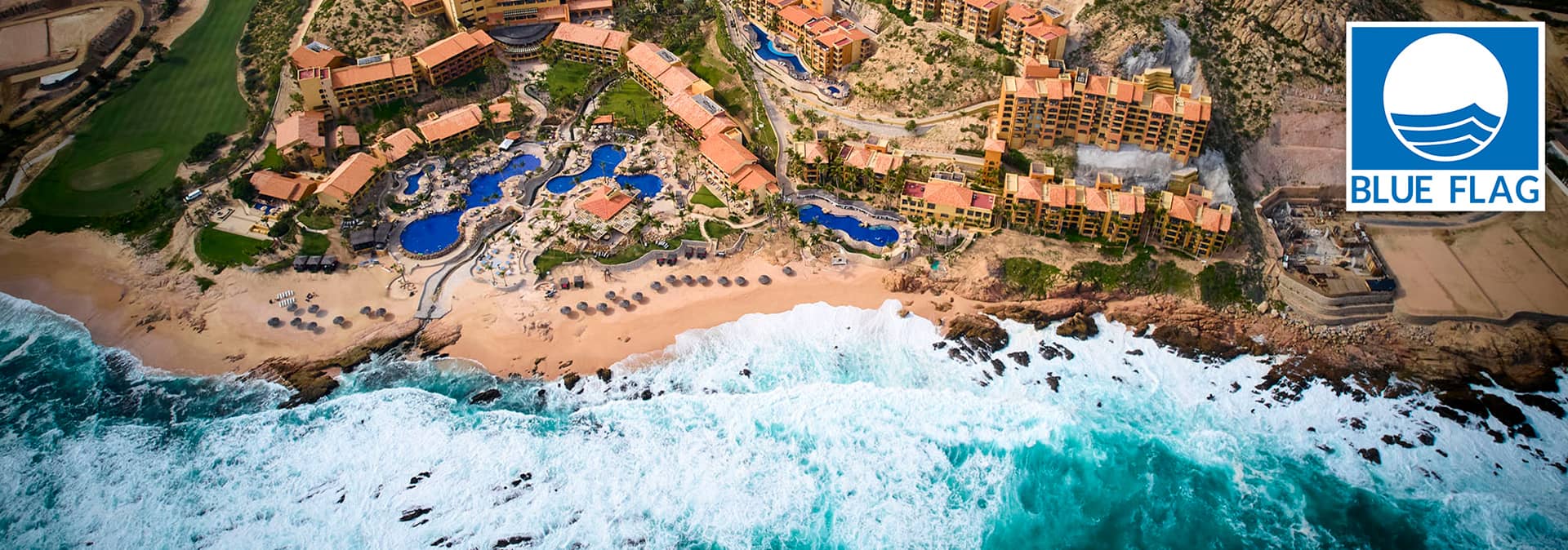 Aerial view of a beachfront resort in Mexico, ideal for meetings and conference events. Multiple pools, sun umbrellas, and oceanfront hotels line the sandy shore. A Blue Flag eco-label logo appears in the top right corner. Waves crash nearby.