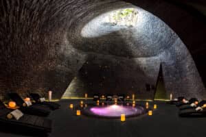 Una sala de spa circular con techo abovedado de piedra, un jacuzzi central iluminado, una suave luz ámbar y sillones reclinables: ideal para relajarse después de eventos y conferencias en los mejores resorts y hoteles de México. Un tragaluz inunda el espacio con luz natural.