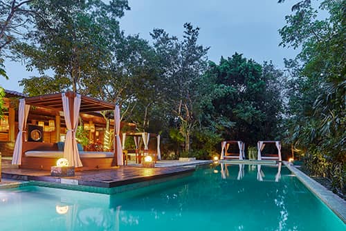 A luxurious outdoor pool at dusk, surrounded by lush trees and greenery, with poolside cabanas featuring draped curtains and soft lighting—an inviting oasis perfect for conference events or relaxing stays at Mexico resorts.