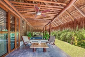 Un patio tropical en uno de los hoteles más exclusivos de México cuenta con techo de paja, vigas de madera, tumbonas, una hamaca, una piscina y exuberante vegetación, perfecto para relajarse entre eventos o reuniones de conferencias.