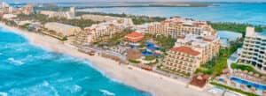 Vista aérea de un complejo turístico frente al mar en México, con varios edificios, piscinas y áreas de descanso a lo largo de una costa arenosa, ideal para conferencias y reuniones, bordeado por un océano turquesa y una exuberante vegetación bajo un cielo despejado.