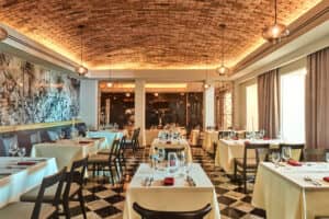 El elegante interior de un restaurante en uno de los hoteles más exclusivos de México cuenta con pisos a cuadros, manteles blancos, servilletas rojas e iluminación tenue, ideal para reuniones o eventos en resorts de lujo. Los grandes ventanales y las obras de arte en las paredes completan la acogedora atmósfera.