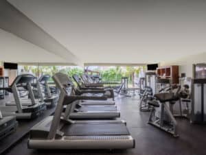 Un gimnasio moderno en uno de los resorts más exclusivos de México, con filas de cintas de correr, máquinas de musculación, grandes espejos y vistas a zonas verdes desde la ventana, perfecto para los huéspedes que asisten a reuniones o conferencias.