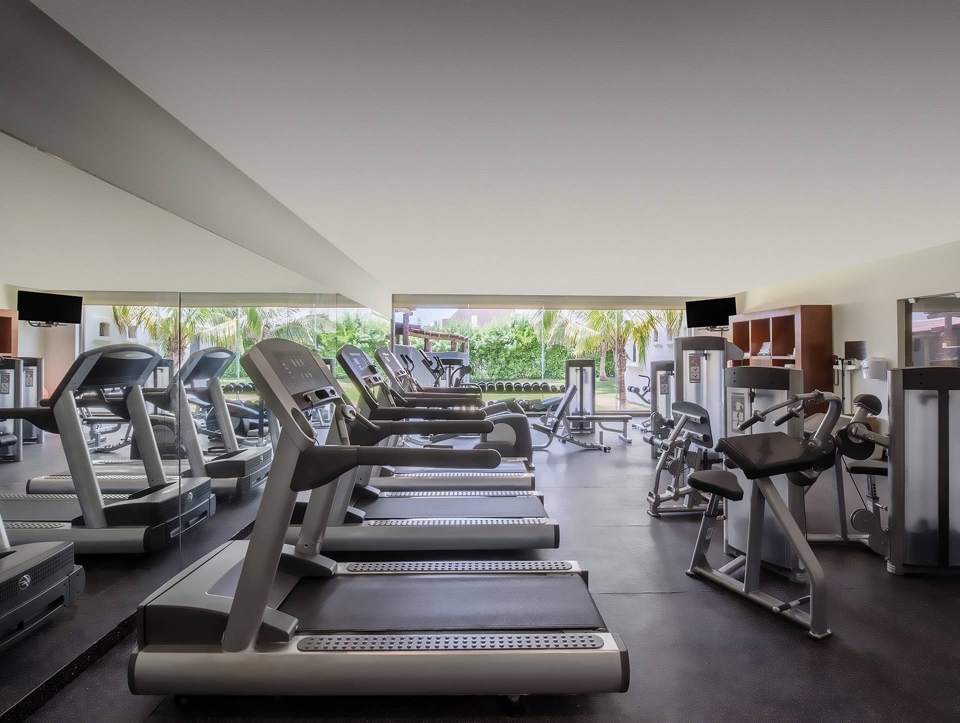 A modern gym at one of Mexico's premier resorts, with rows of treadmills, strength machines, large mirrors, and a window view of greenery—perfect for guests attending meetings or conference events.