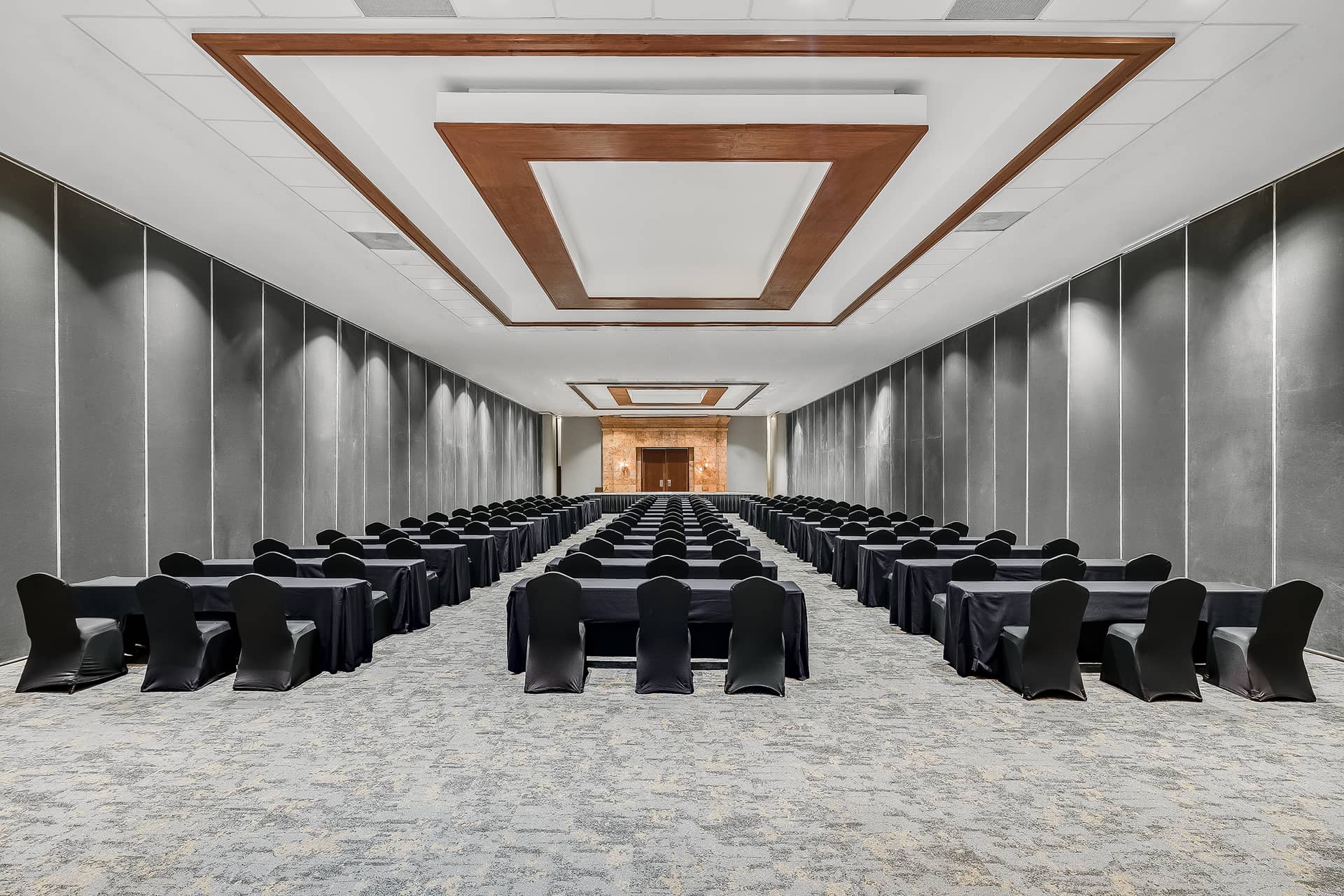 A large, modern conference room at one of Mexico’s top resorts, with rows of tables and black-covered chairs arranged classroom-style facing a stage. Geometric ceiling designs and neutral-toned walls create an ideal setting for meetings or conference events.