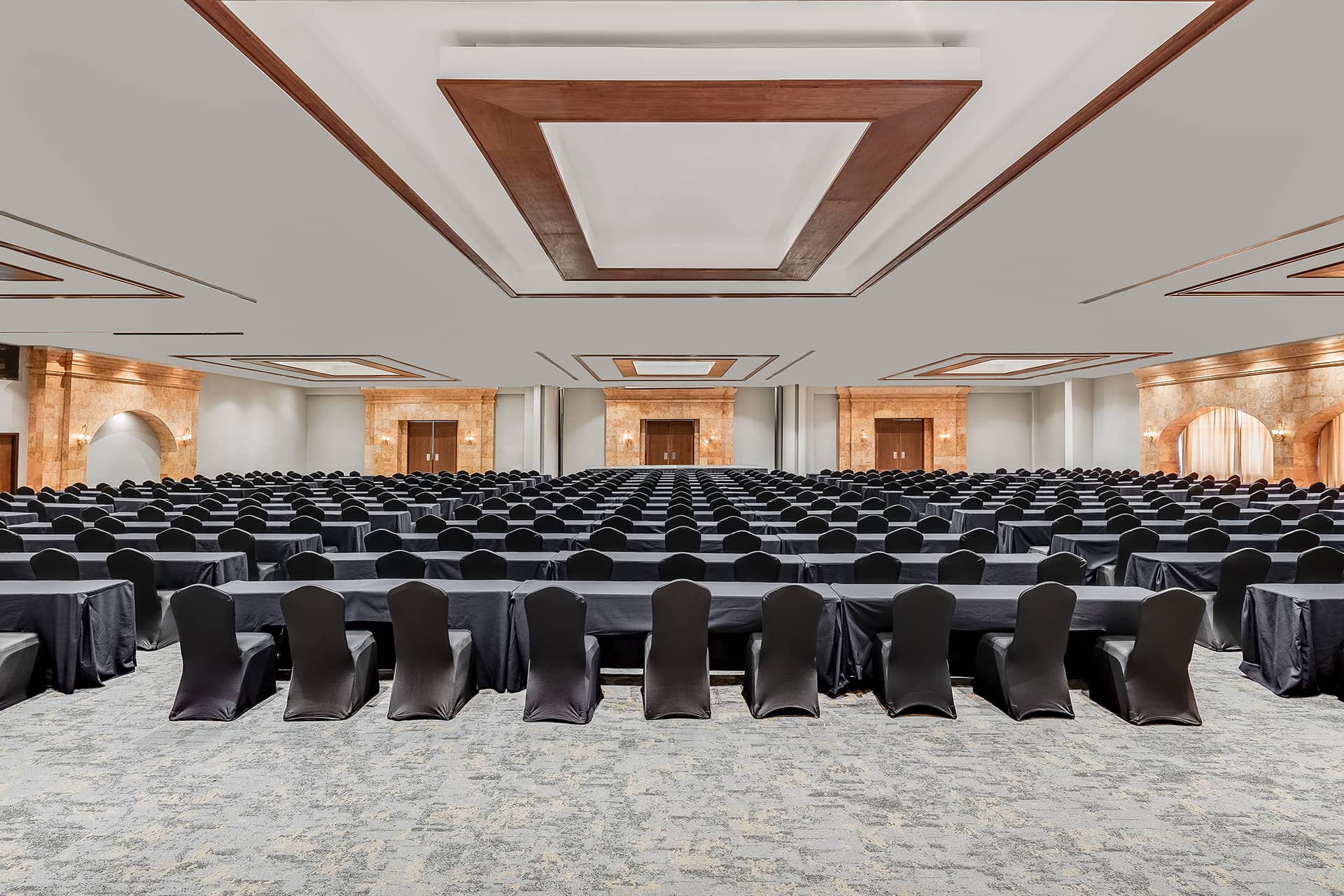 A large, elegant conference hall at one of Mexico’s top resorts, set up for meetings and conference events with rows of tables and black covered chairs facing a stage, under modern geometric ceiling panels and warm ambient lighting.