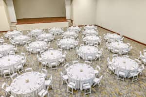 Un amplio salón de banquetes en uno de los resorts más exclusivos de México, con mesas redondas cubiertas con manteles blancos, cada una preparada para reuniones y conferencias. Las mesas están espaciadas uniformemente y hay un escenario al frente de la sala.