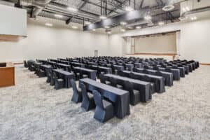 Amplia sala de conferencias en uno de los resorts más exclusivos de México, con filas de mesas y sillas cubiertas con manteles negros frente a un escenario. Ideal para reuniones o eventos, el espacio cuenta con conductos de ventilación a la vista e iluminación industrial en el techo.
