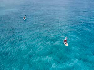 Vista aérea de dos personas en aguas cristalinas en uno de los mejores resorts de México; una persona practica paddleboard en primer plano, mientras que la otra rema en kayak más lejos, al fondo. Ideal para conferencias y reuniones.