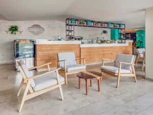 Un acogedor rincón de café con cuatro sillas de madera clara alrededor de una pequeña mesa de madera, sobre un suelo de baldosas; perfecto para reuniones informales en hoteles de México o eventos de conferencias, con plantas y equipo de café que realzan el ambiente acogedor.