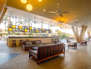 Bar y salón moderno al aire libre con muebles de madera, ventiladores de techo, iluminación decorativa y palmeras visibles en el exterior: perfecto para eventos de conferencias relajados o reuniones informales en los mejores hoteles turísticos de México.