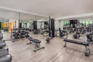 Un gimnasio espacioso en los resorts de México con piso de madera, espejos, pesas libres, bancos, máquinas de resistencia, cintas de correr, elípticas y grandes ventanales que dejan entrar la luz natural, perfecto para los huéspedes que asisten a conferencias o reuniones.
