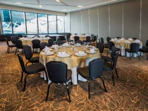 El salón de banquetes de este complejo turístico en México es ideal para conferencias o reuniones, con mesas redondas preparadas para una comida formal, sillas negras y grandes ventanales que dejan entrar la luz natural.