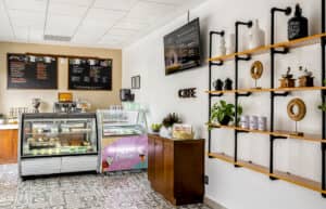 Un acogedor interior de cafetería con suelos de baldosas estampadas, una vitrina para pasteles, un congelador de helados, menús en pizarra y un televisor montado en la pared: perfecto para reuniones informales o para relajarse después de eventos de conferencias en hoteles y complejos turísticos de México.