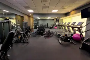 Un moderno gimnasio en uno de los resorts más exclusivos de México, equipado con cintas de correr, bicicletas estáticas, pesas y balones de ejercicio sobre un elegante suelo negro. Grandes espejos reflejan el espacio, ideal para huéspedes que asisten a reuniones o conferencias.