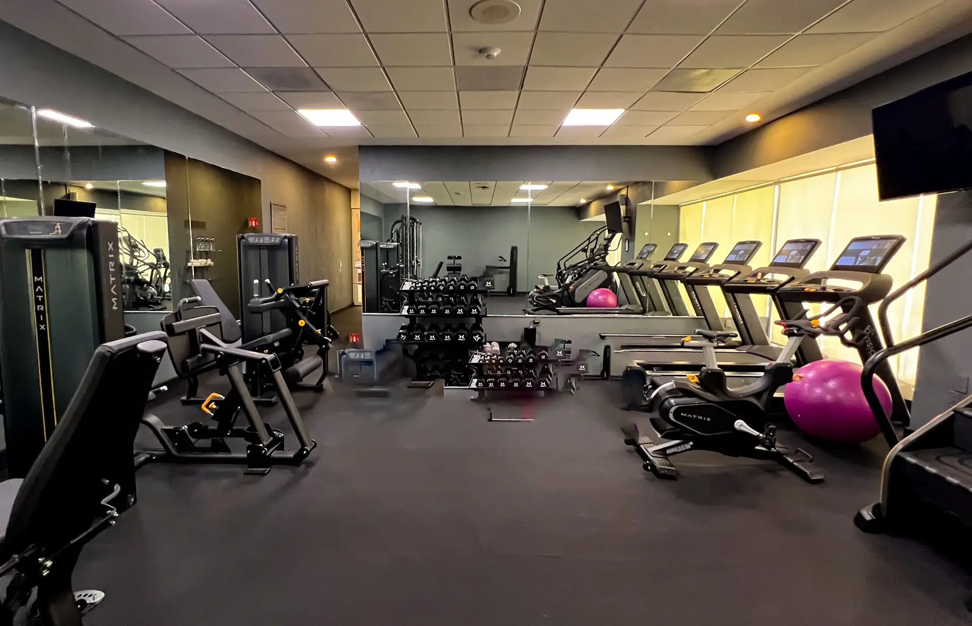 A modern gym at one of Mexico’s top resorts, featuring treadmills, bikes, weights, and exercise balls on a sleek black floor. Large mirrors reflect the space—ideal for guests attending meetings or conference events.