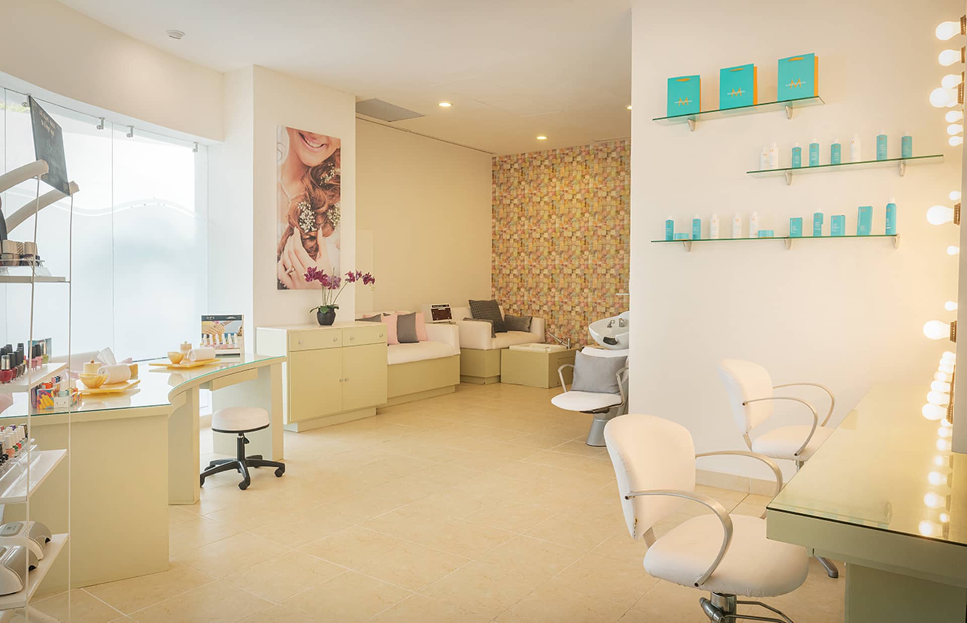 A modern, brightly lit beauty salon in one of Mexico’s top resorts, featuring styling chairs, mirrors, shelves of hair products, a manicure table, and a cozy seating area. The inviting decor includes soft colors and a floral accent wall.