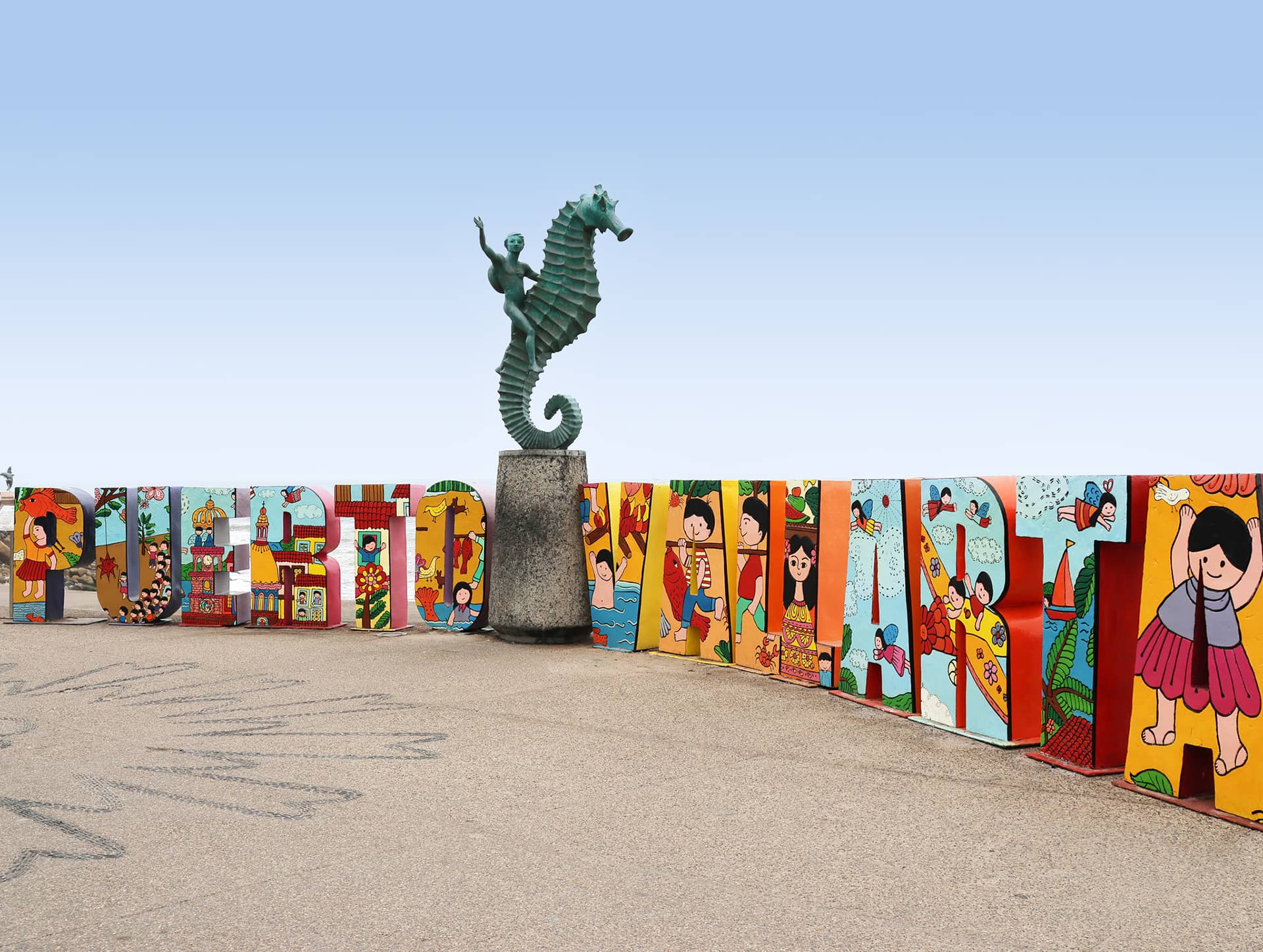 Colorful Puerto Vallarta sign with vibrant illustrations, located on a seaside promenade near top Mexico hotels. A bronze statue of a boy riding a seahorse stands behind the sign, under a clear blue sky—perfect for conference events or meetings.