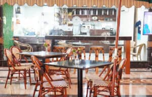 Una acogedora cafetería con varias mesas vacías y sillas de mimbre, pequeños jarrones de flores como centros de mesa y una barra con equipo de café al fondo: perfecta para reuniones informales en los centros turísticos de México, que ofrece un ambiente cálido y acogedor.