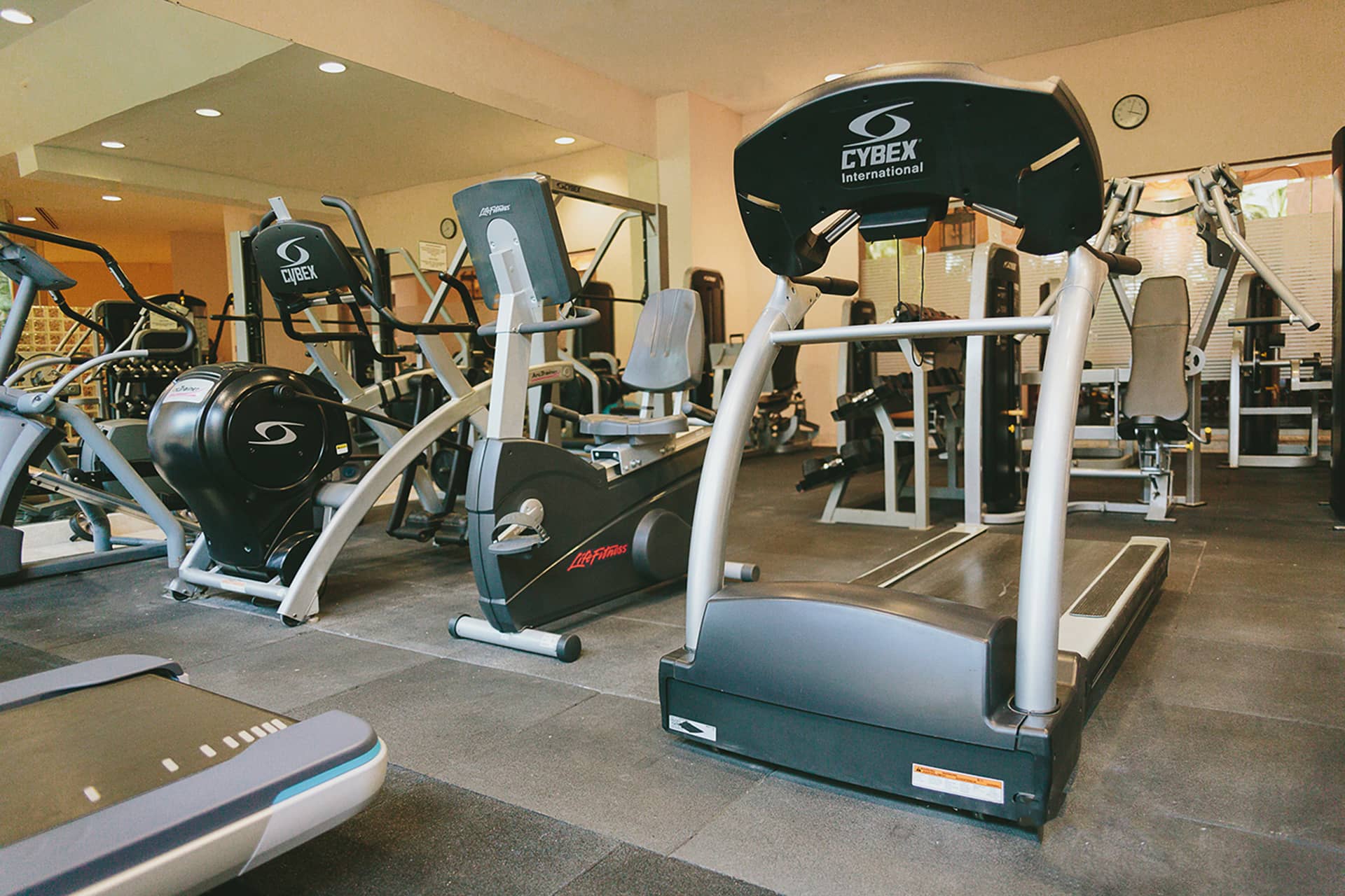 A gym with various exercise machines, including treadmills, stationary bikes, and elliptical trainers, arranged neatly on a rubber floor with mirrors and bright lighting—perfect for guests at Mexico hotels hosting meetings or conference events.