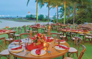 En los complejos turísticos de México, se puede disfrutar de comidas al aire libre junto a la playa, con mesas redondas de madera decoradas con servilletas rojas, flores y velas, rodeadas de sillas de madera, palmeras y guirnaldas de luces; un espacio perfecto para conferencias o reuniones junto al mar.