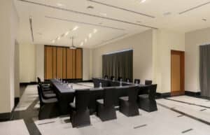 Una moderna sala de conferencias en uno de los mejores complejos turísticos de México, con una disposición de mesas en forma de U, sillas negras, agua embotellada en cada asiento, un proyector de techo y paredes de colores neutros, ideal para reuniones y eventos.
