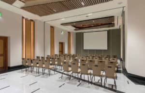 Una moderna sala de conferencias en uno de los resorts más exclusivos de México, con filas de sillas beige frente a una gran pantalla de proyección. Los detalles en madera, los techos altos con iluminación empotrada y los pisos pulidos crean un ambiente ideal para reuniones y eventos.