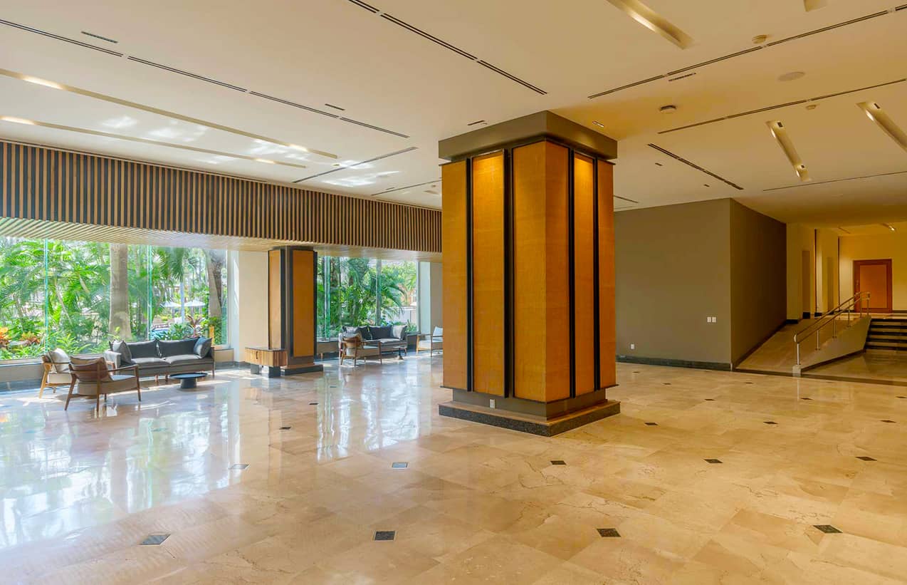 Spacious hotel lobby with marble floors, a large central pillar, and modern seating areas by tall windows—ideal for conference events. Neutral tones and abundant natural light create an inviting atmosphere at one of Mexico's premier resorts.