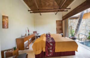 Una serena sala de tratamientos de spa con dos camillas cubiertas con sábanas amarillas y rojas, muebles modernos de madera y una puerta abierta que da a una piscina privada: perfecta para relajarse entre eventos de conferencias en complejos turísticos u hoteles en México.