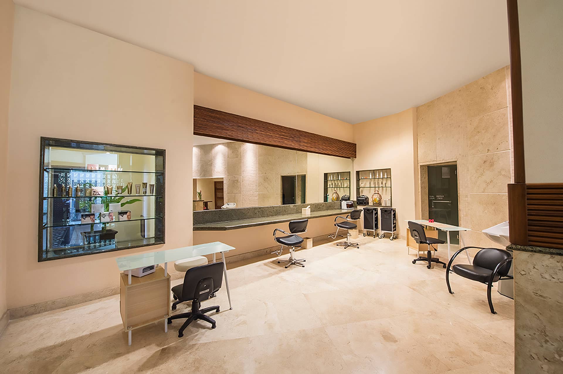 Bright, modern salon with three workstations, black chairs, mirrors, and light marble floors—ideal for conference events or meetings at resorts. Shelves with products and a large window reflecting the outdoors create an uncluttered, inviting space.