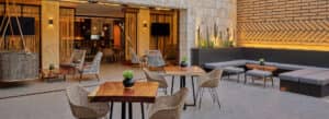 Los patios al aire libre de los resorts mexicanos cuentan con modernas sillas de mimbre, mesas de madera con plantas en macetas, bancos acolchados, paredes de ladrillo y piedra, y una vista abierta a un salón interior, perfectos para reuniones o eventos de conferencias en los mejores hoteles.