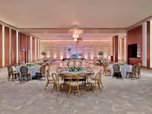 Amplio y elegante salón de banquetes en uno de los resorts más exclusivos de México, con mesas y sillas redondas, tonos neutros, iluminación tenue, una pared decorativa de piedra, grandes centros de mesa florales y una moderna lámpara de araña: perfecto para reuniones o eventos de conferencias.
