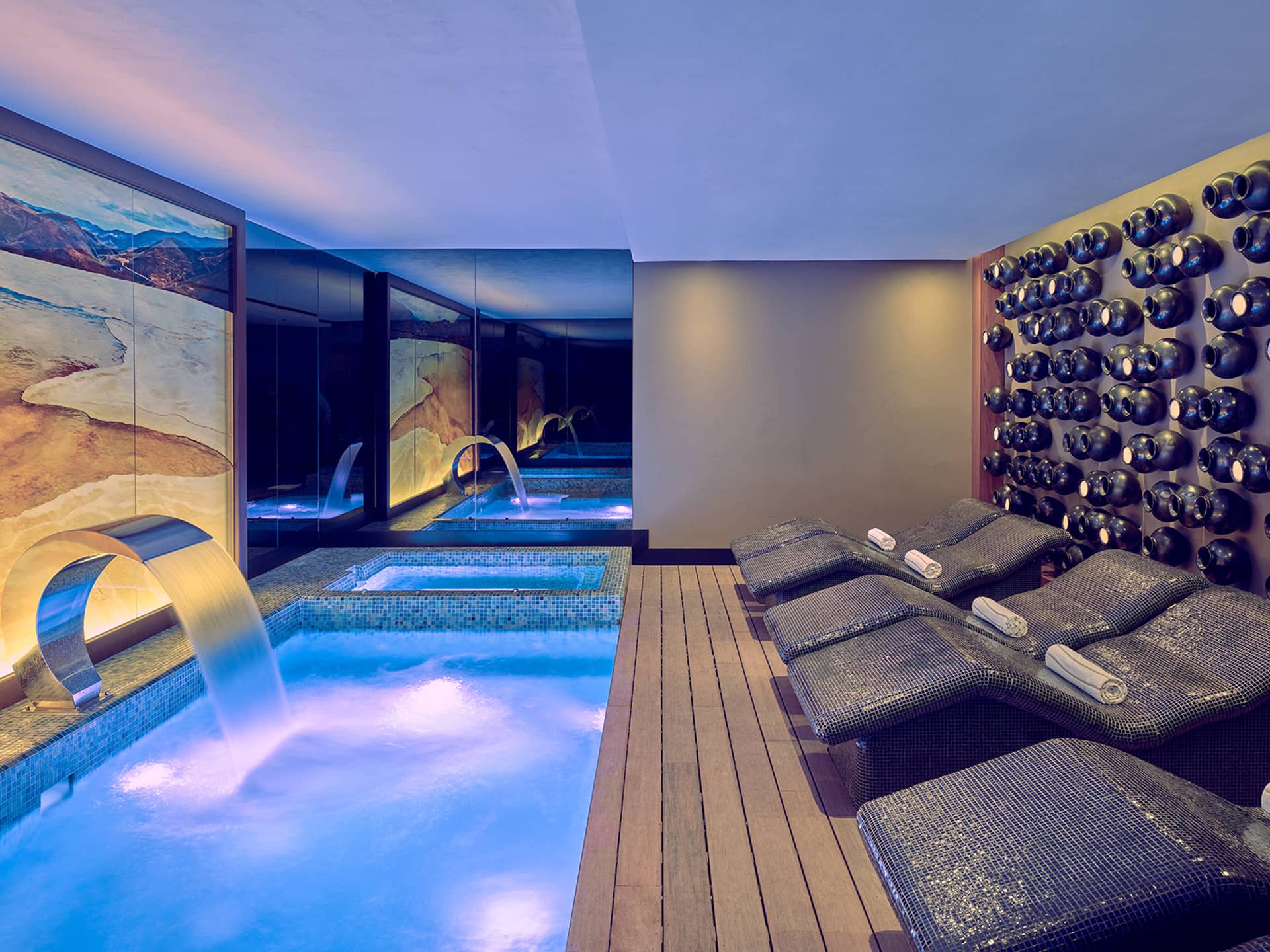 Modern spa room in one of Mexico’s top resorts, featuring an illuminated pool, water fountain feature, and mosaic-tiled lounge chairs. Perfect for unwinding after conference events or meetings, with art and dark stones fostering relaxation.