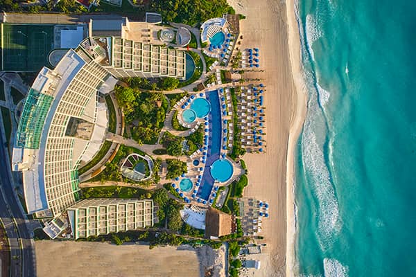 Aerial view of a large beachfront resort in Mexico with multiple pools, lounge chairs, and lush landscaping—perfect for conference events or meetings by the sandy beach and turquoise ocean waves.