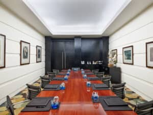 Una moderna y luminosa sala de conferencias en uno de los resorts más exclusivos de México, equipada con una larga mesa de madera, sillas negras, blocs de notas, bolígrafos y vasos de agua, ideal para reuniones o eventos. Obras de arte enmarcadas y una estación de refrigerios completan el espacio.
