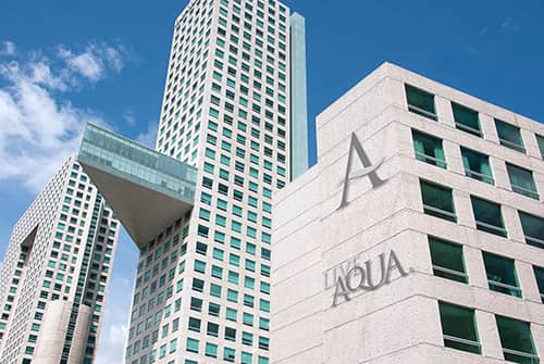 Modern high-rise hotels with geometric designs and many windows, including one with a distinctive protruding horizontal structure, rise under a clear blue sky. The word AQUA is visible on the nearest building—an ideal spot for meetings or conference events.