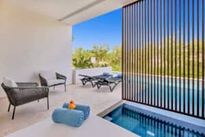 Un moderno patio al aire libre en uno de los mejores resorts de México, que cuenta con una pequeña piscina, tumbonas, sillones, una mesa con toallas azules enrolladas y un patito de goma, y ​​una mampara para mayor privacidad; ideal para relajarse entre reuniones o eventos de conferencias.