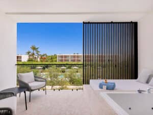 Un moderno balcón de hotel con zona de estar, sillas y jacuzzi ofrece vistas a una piscina, árboles y otros edificios; perfecto para relajarse después de eventos de conferencias en los mejores complejos turísticos de México.