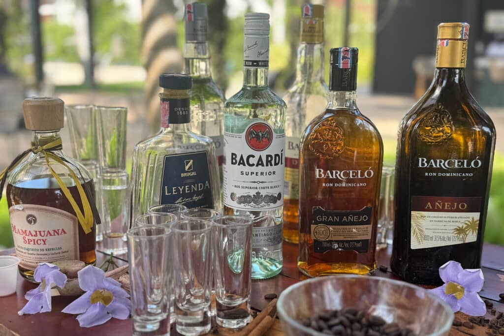 A variety of rum bottles, including Mamajuana, Leyenda, Bacardi, and Barceló, are arranged on a table with shot glasses, flowers, cinnamon sticks, and coffee beans—perfect for conference events or meetings at Mexico resorts and hotels.