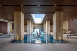Lujosa piscina cubierta con cuatro pilares de piedra, techo de madera, tragaluz, tumbonas junto a la piscina con toallas y una iluminación elegante: perfecta para relajarse después de eventos o reuniones en hoteles y complejos turísticos de lujo en México.
