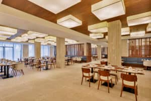 Un restaurante amplio y moderno en uno de los mejores hoteles de México, con mesas y sillas de madera, suelo de baldosas beige, grandes lámparas de techo y ventanales que van del suelo al techo: un entorno ideal para reuniones o eventos de conferencias.