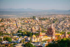 Una vista panorámica de San Miguel de Allende, México, con sus coloridos edificios, exuberante vegetación y la emblemática Parroquia de San Miguel Arcángel: un telón de fondo inspirador para conferencias o reuniones en los mejores hoteles y resorts de México.